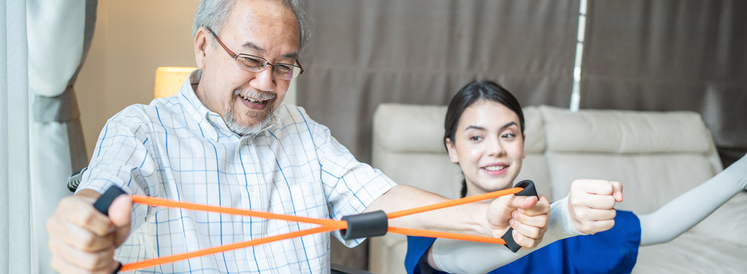 Asian man in glasses and a wheelchair works with therapist on stretch bands