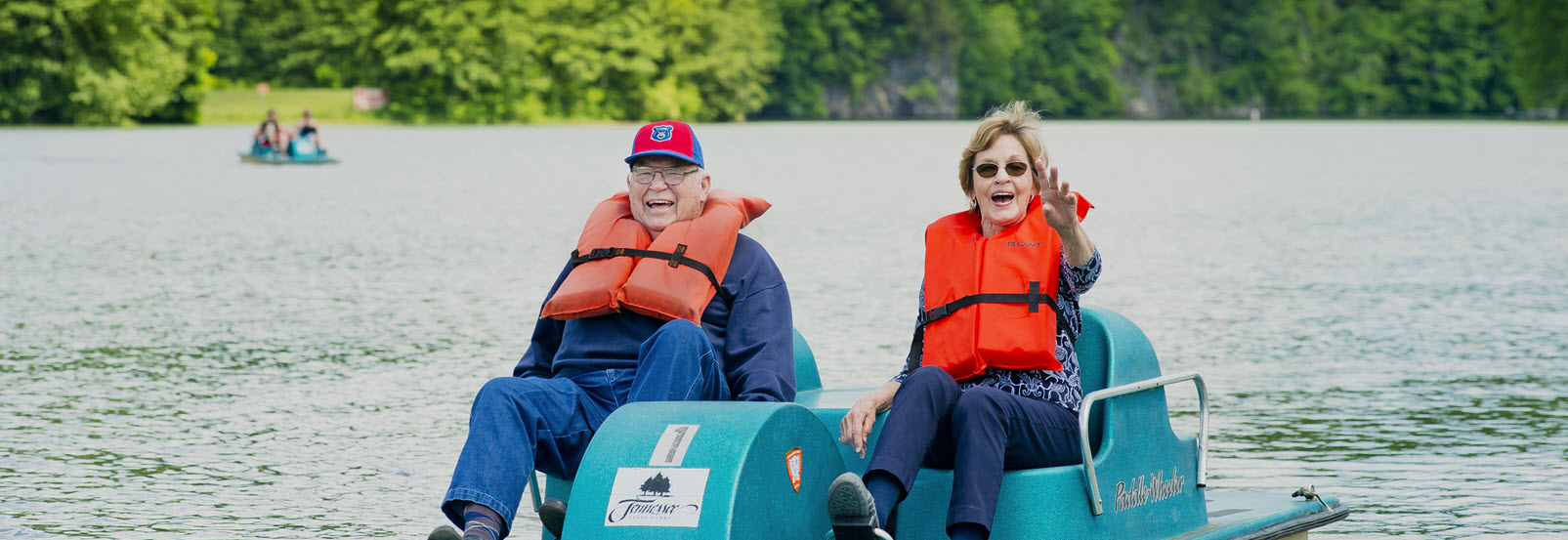 senior man and woman laugh and wave from a paddle boat in Kingsport, Tenn. state park.
