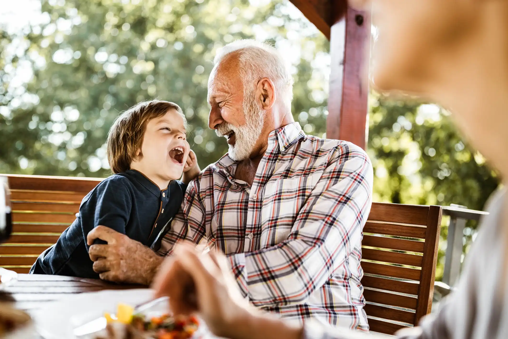 Older man smiling and laughing with a young child while sitting together outdoors